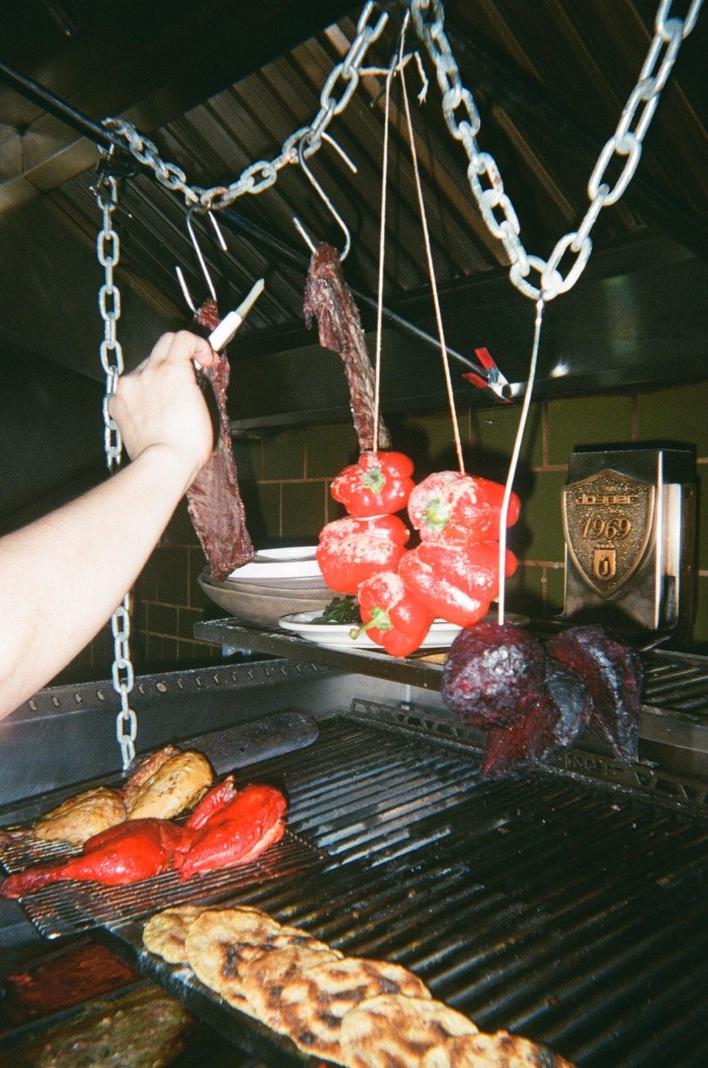 Cortes de carne y pimientos asados colgando de los ganchos sobre el asador