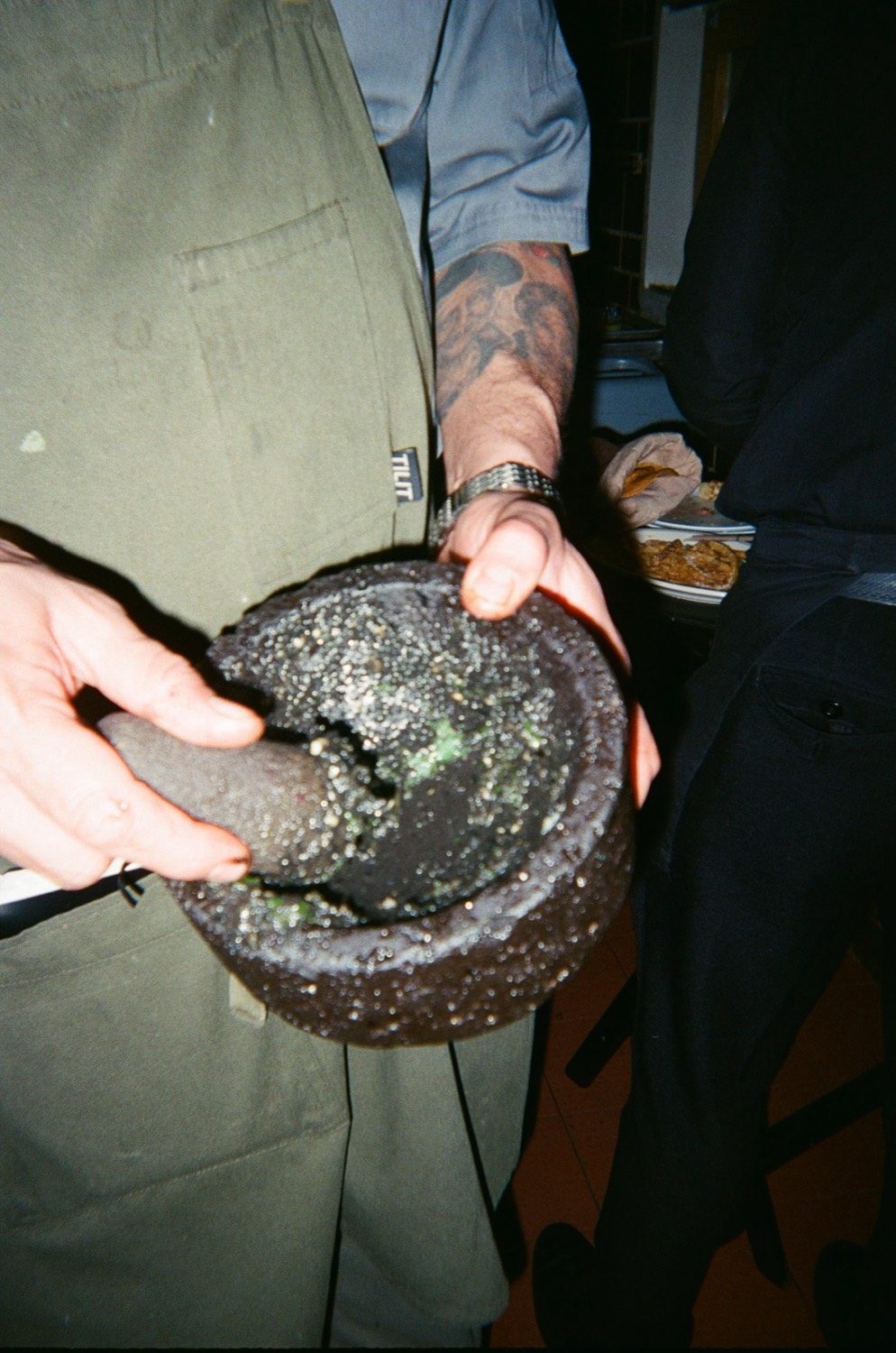 Dos cocineros se pasan un molcajete de piedra con salsa verde