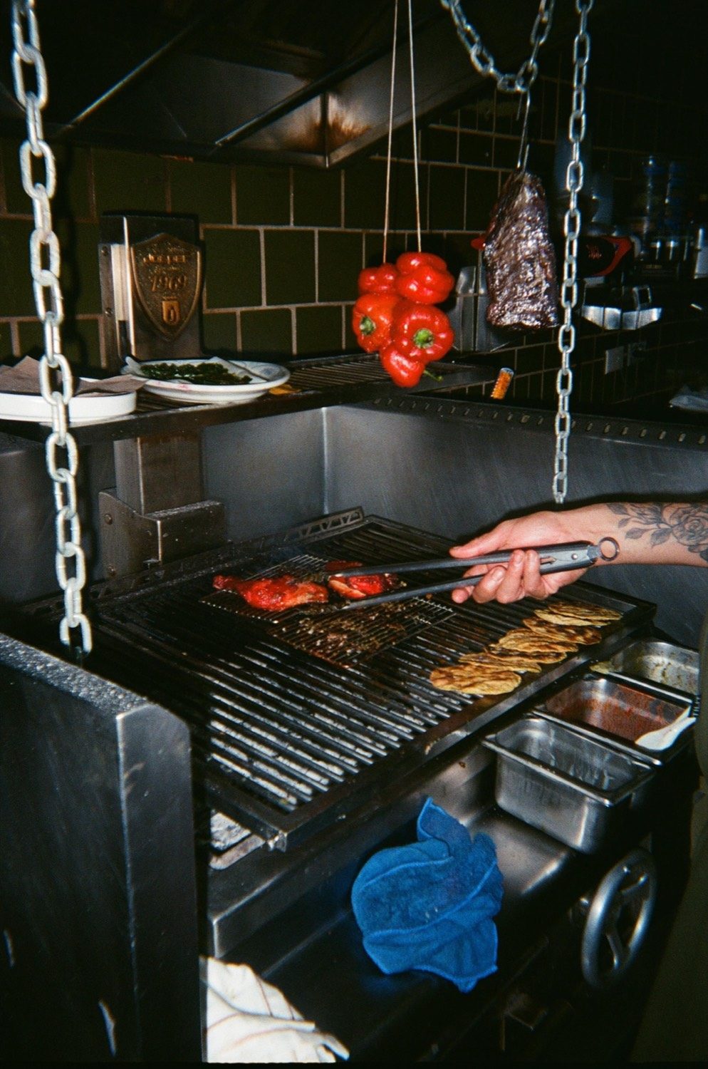 Unas tenazas voltean pimientos sobre las brasas del asador de leña